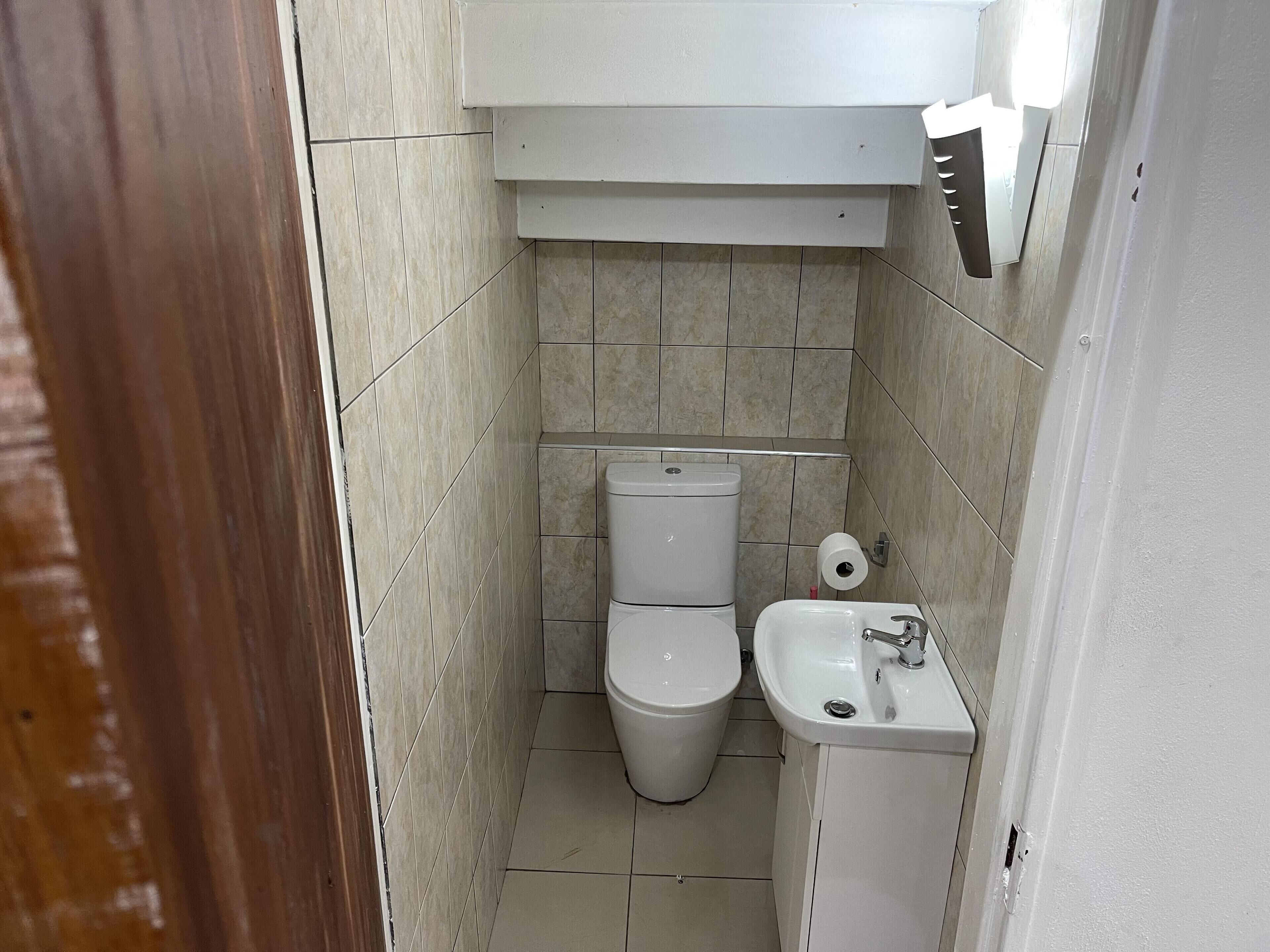 A small, tiled bathroom with a toilet, sink, and a toilet paper holder.