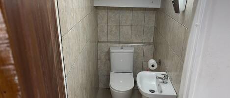 A small, tiled bathroom with a toilet, sink, and a toilet paper holder.