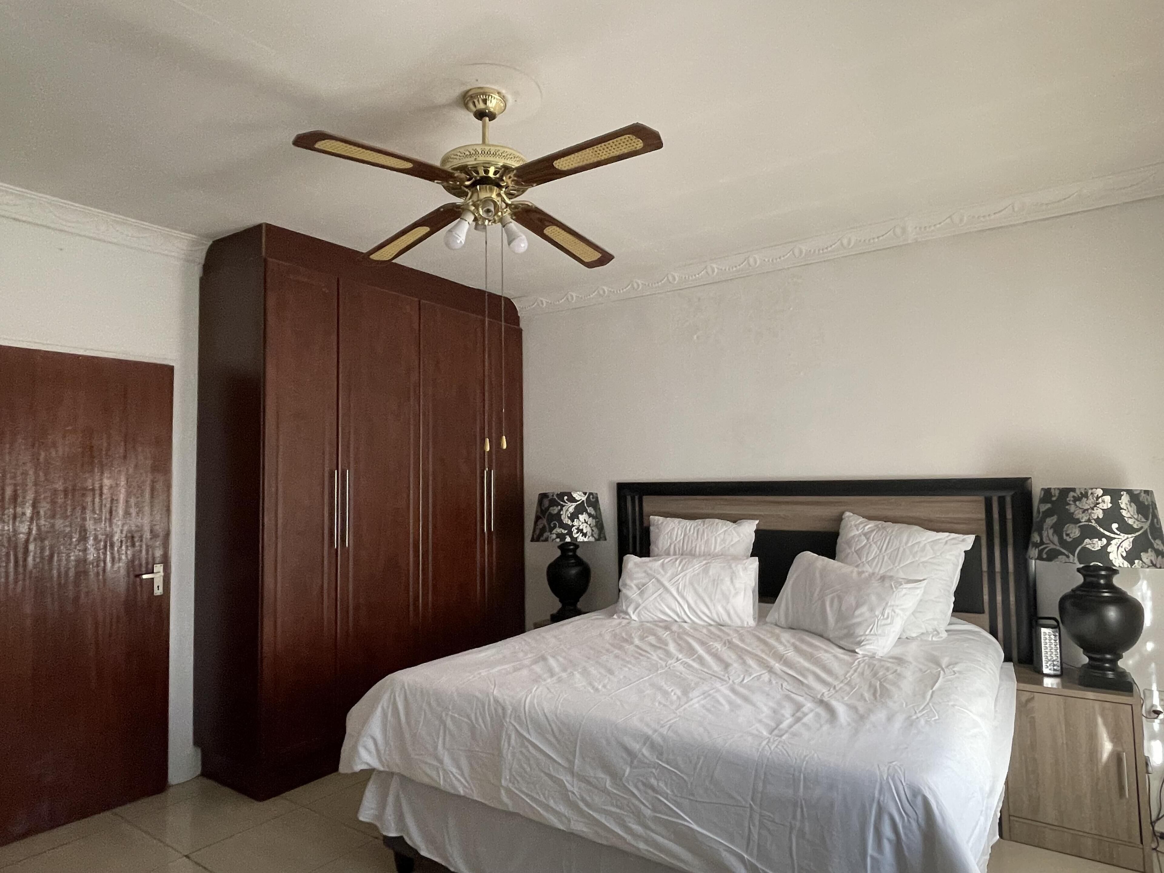 A bedroom with a bed, a wardrobe, a ceiling fan, and bedside lamps.