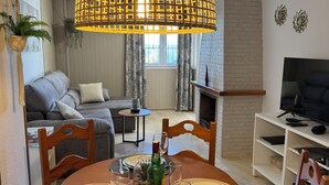 A dining area with a round table set for four, a bottle of wine, and a TV in the background.