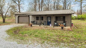 A single-story house with a garage, a front porch with seating, and a small garden area. - Roos&Blues lake house. City park steps away. Rm for 6, king beds, pets friendly (Madisonville)