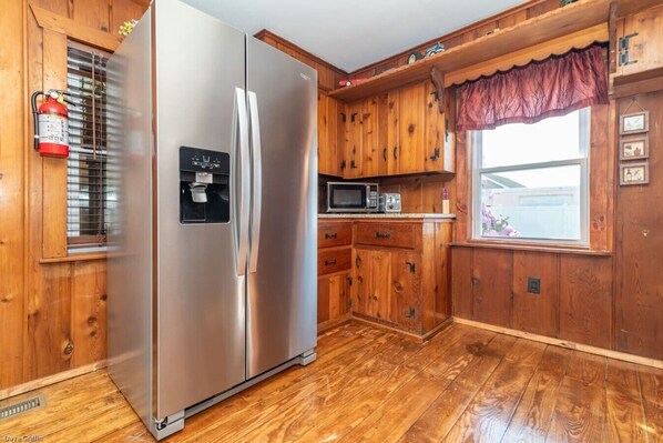 A kitchen with wooden cabinets, a stainless steel refrigerator, a microwave, and a window with a view.