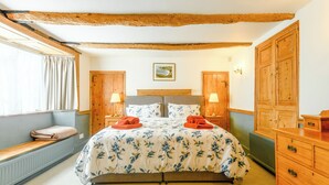 Een slaapkamer met een houten bed, twee nachtkastjes met lampen, een houten kledingkast en een raam met gordijnen.