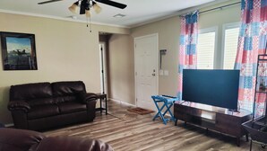 Un salon avec un canapé en cuir marron, un téléviseur posé sur un meuble, un ventilateur de plafond et une porte donnant sur une autre pièce.
