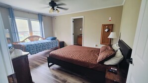 A bedroom with two beds, a ceiling fan, a wooden dresser, and a window with blinds.