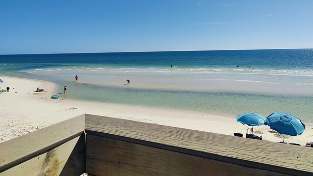 A beach with clear skies, a wooden deck, and two blue umbrellas.
