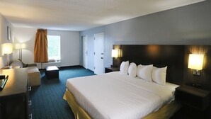 Una habitación de hotel con una cama grande, un escritorio con lámpara, una silla, una ventana con cortinas y una puerta.