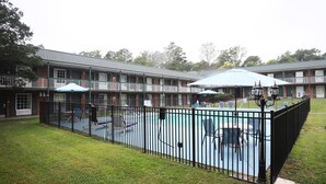 Un hotel con zona de piscina cercada, mobiliario exterior y un patio cubierto.