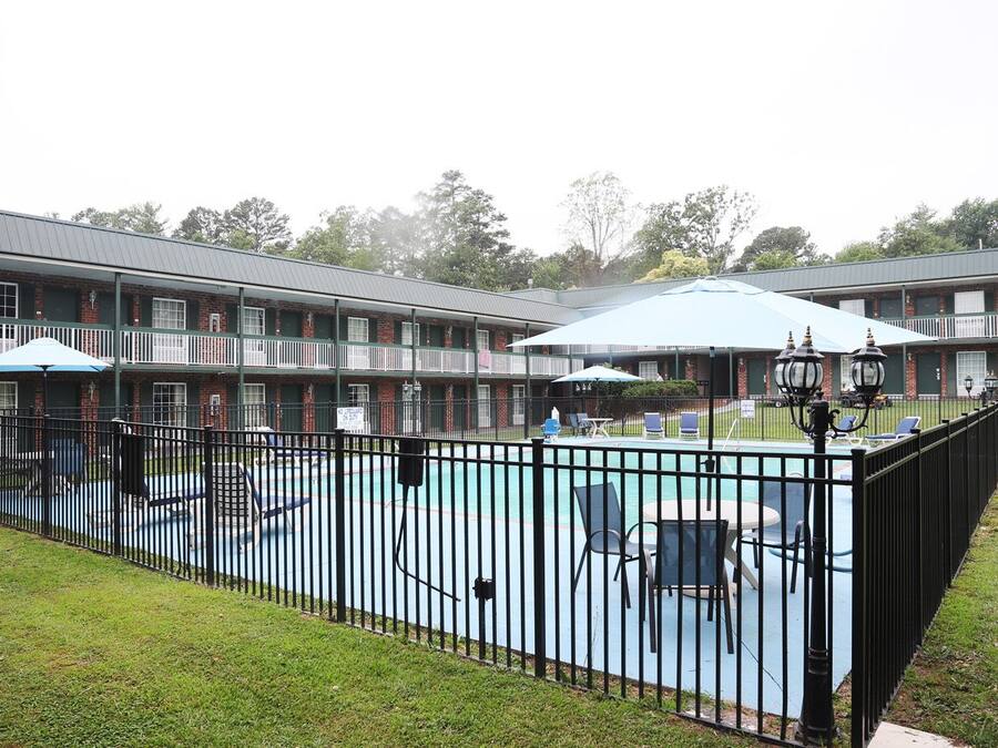 A hotel with a fenced pool area, outdoor seating, and a covered patio.