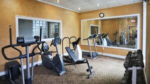 Un gimnasio con diverso equipamiento de ejercicio, un espejo grande y un reloj en la pared.