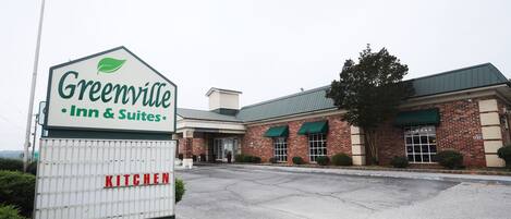 Um edifício de tijolos com toldo verde e um letreiro que diz 'Greenville Inn & Suites'.