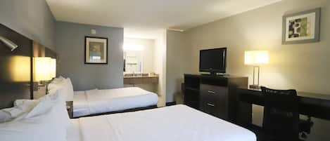 Ein Hotelzimmer mit zwei Betten, einem Schreibtisch, einem Fernseher und einer Lampe.