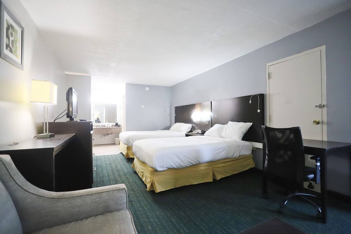 Habitación de hotel con dos camas, un escritorio, una silla, una lámpara de escritorio, una computadora y una puerta.