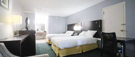 A hotel room with two beds, a desk, a chair, a desk lamp, a computer, and a door.
