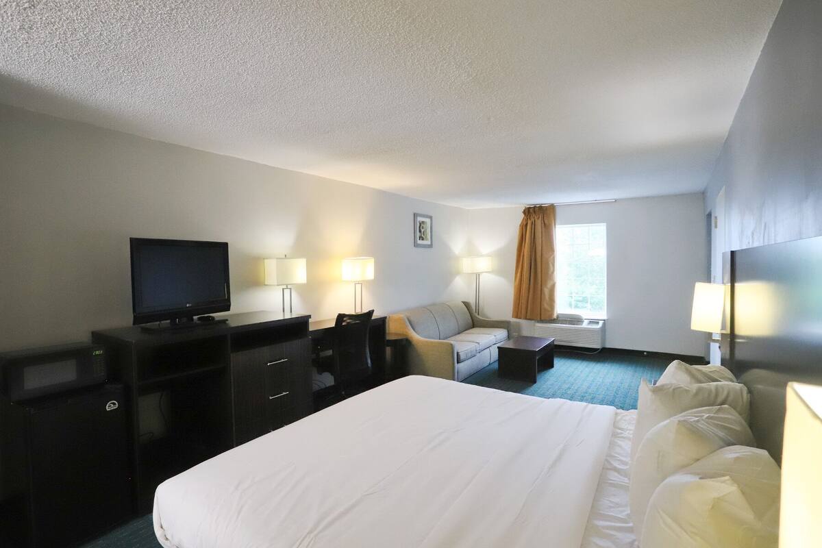 Habitación de hotel con cama, escritorio, televisión, dos lámparas, sofá y ventana con cortinas.