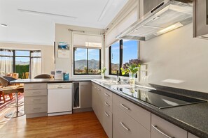 A modern kitchen with a large window, a dishwasher, and a dining area with a view of mountains. - Selmes Sanctuary - Blenheim Holiday Home (Blenheim)