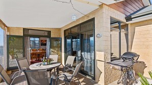 Een terras met een tafel en stoelen, een barbecue en een glazen deur naar een binnenruimte.
