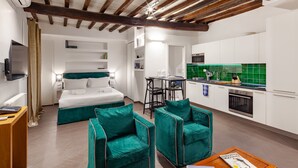 A modern hotel room with a bed, two green armchairs, a wooden coffee table, a desk, and a kitchenette with a green backsplash. - Annamaria House at the Pantheon (Roma)