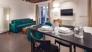 A dining area with a table set for four, a teal sofa, and a television mounted on the wall. - Annamaria House at the Pantheon (Roma)