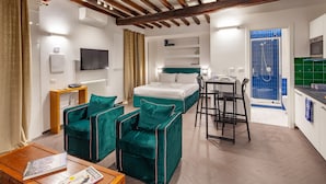 A modern hotel room with a bed, two green armchairs, a wooden table, a TV, and a kitchenette. - Annamaria House at the Pantheon (Roma)