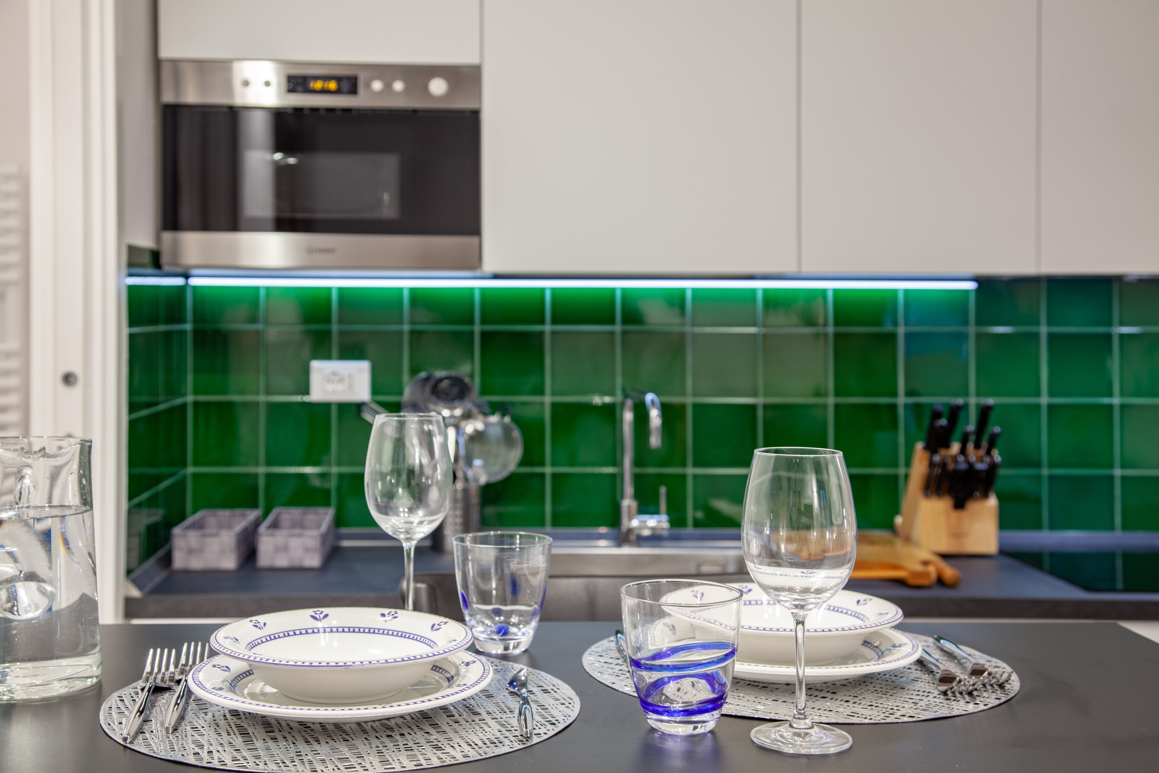 Una cocina con una mesa de comedor dispuesta para dos personas, con platos, vasos y cubiertos.
