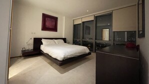 A modern bedroom with a bed, a nightstand, a desk, and a large window offering a city view. - Stunning View 2 Bed Apartment - Canary Wharf City (London)