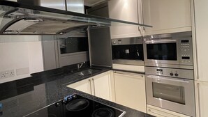 A modern kitchen with stainless steel appliances, a black countertop, and white cabinetry. - Stunning View 2 Bed Apartment - Canary Wharf City (London)
