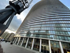 Een modern hoogbouwgebouw met een gebogen glazen gevel, grote ramen en een opvallende metalen constructie op de voorgrond.