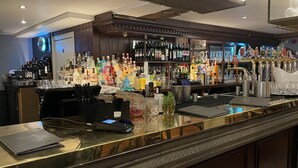 A bar area with a polished counter, various bottles, glasses, and a cash register. - Stunning View 2 Bed Apartment - Canary Wharf City (London)