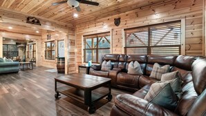 A log cabin interior with a leather sofa, wooden flooring, and a ceiling fan. - Family Cabin, 3 King Suites, Game Room, Hot Tub, Minutes to Dollywood (Pigeon Forge)