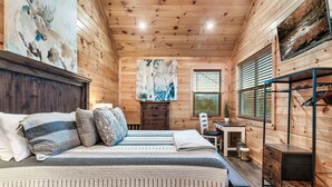 A cozy wooden cabin room with a bed, a desk, and a chair. - Family Cabin, 3 King Suites, Game Room, Hot Tub, Minutes to Dollywood (Pigeon Forge)