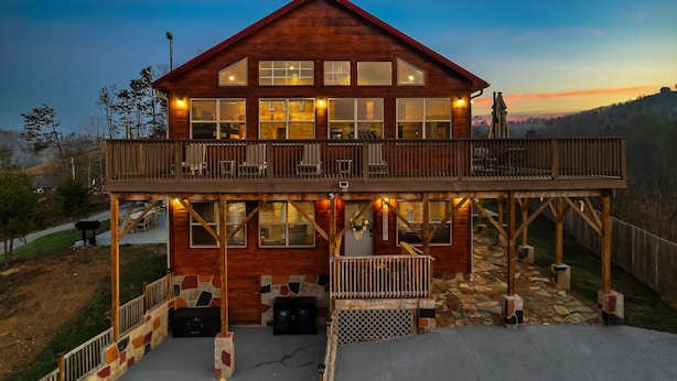 A two-story wooden cabin with a balcony, stone foundation, and a view of the surrounding landscape. - Family Cabin, 3 King Suites, Game Room, Hot Tub, Minutes to Dollywood (Pigeon Forge)