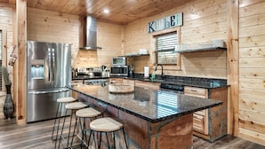 A modern kitchen with wooden walls, stainless steel appliances, a granite countertop, and a central island with stools. - Family Cabin, 3 King Suites, Game Room, Hot Tub, Minutes to Dollywood (Pigeon Forge)
