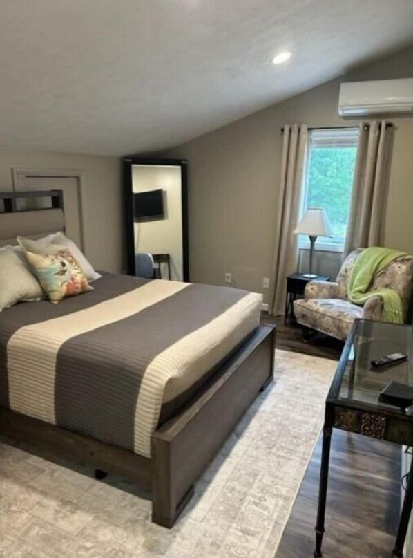 Relax in this serene bedroom with a large bed, bedside table, and large window with curtains.