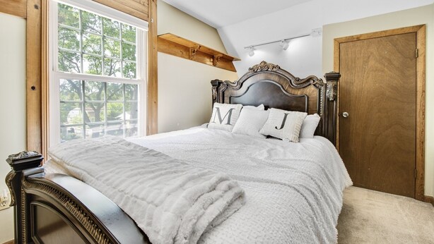 Una camera da letto con un letto grande, una testiera in legno, una finestra vista alberi e una porta.