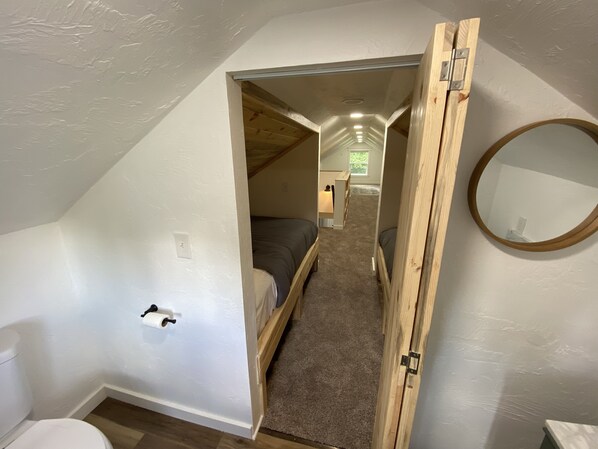 A narrow, sloped ceiling room with a bed, a wooden door, and a mirror.