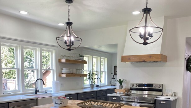 A modern kitchen with a wooden island, bar stools, stainless steel appliances, and large windows.