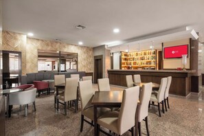A hotel lobby with a bar area, seating arrangements, and a television screen.