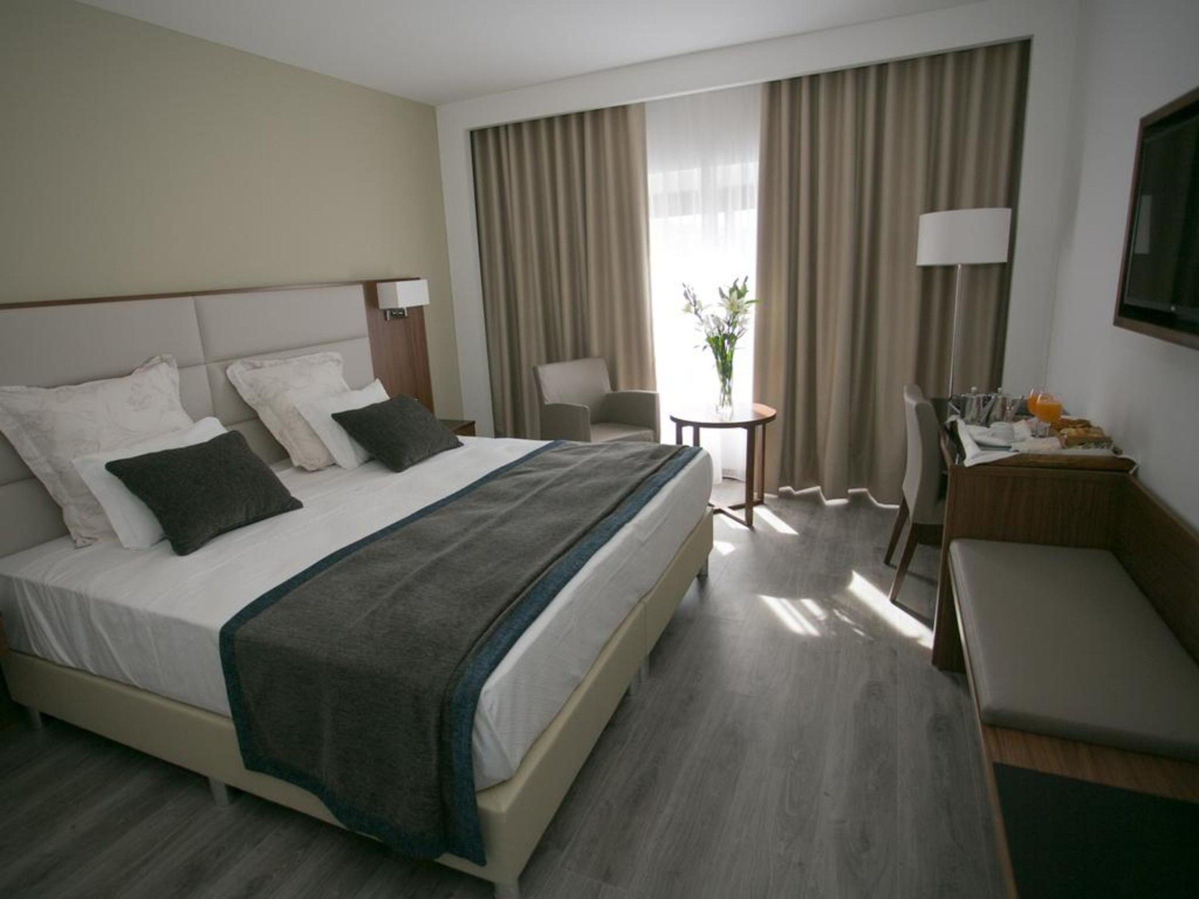 A hotel room with a bed, bedside tables, a desk, a chair, and a window with curtains.