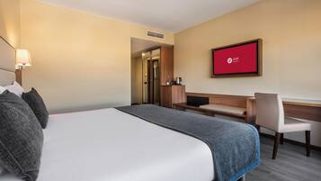 Een hotelkamer met een bed, een bureau, een stoel, een televisie en een minibar.