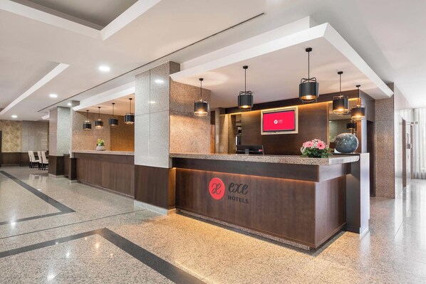 A hotel reception area with a modern design, featuring a reception desk, seating area, and a digital display.