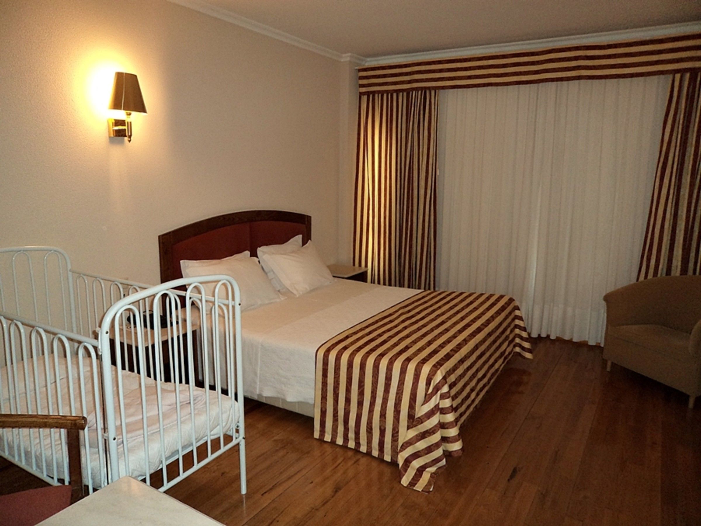 A hotel room with a bed, a chair, a bedside table, a lamp, and a window with curtains.