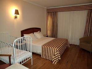 A hotel room with a bed, a chair, a bedside table, a lamp, and a window with curtains. - Exe São Lázaro (Braganca)