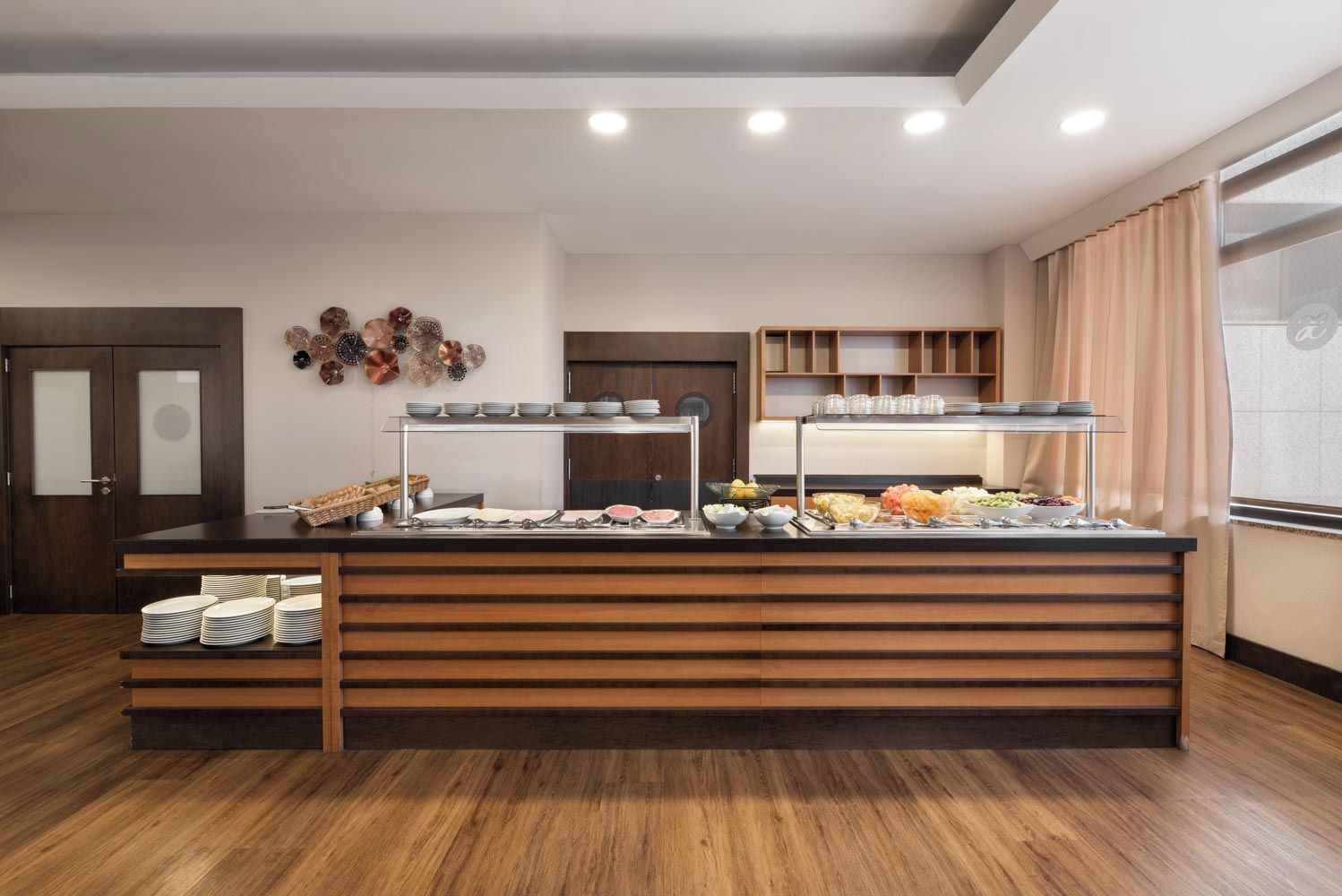 Disposição de buffet com várias estações de serviço, balcão de madeira e exposição de pratos e tigelas fixada na parede.