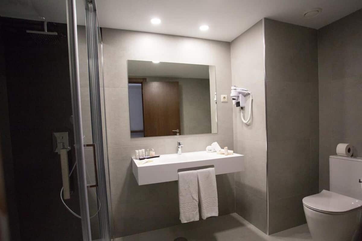 A modern bathroom with a glass shower enclosure, a white sink with toiletries, a mirror, and a toilet.