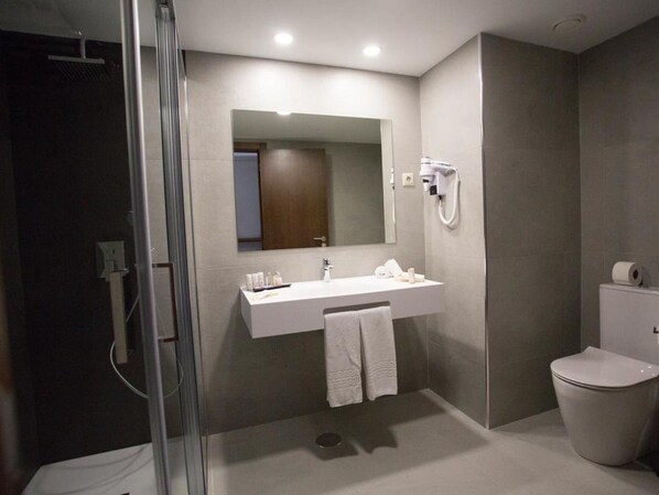 A modern bathroom with a glass shower enclosure, a white sink with toiletries, a mirror, and a toilet.