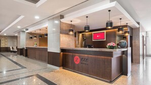 Et hotellets receptionsområde med et moderne design, der inkluderer en receptionsdisk, siddeområde og en digital skærm.