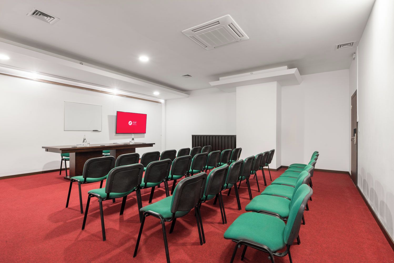 Una sala de conferències amb una taula llarga, files de cadires, una pantalla de projector i una pissarra.