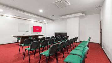 Una sala de conferències amb una taula llarga, files de cadires, una pantalla de projector i una pissarra.