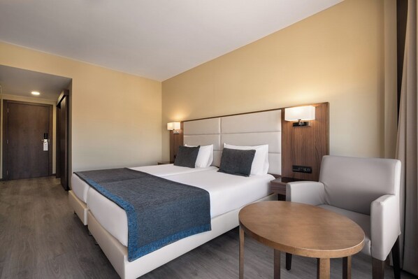 Una habitación de hotel con una cama grande, una mesita de noche, una silla y una pequeña mesa.